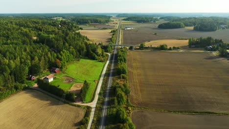High-altitude-aerial-drone-view-moving-backwards-following-above-long-straight-electrified-railroad-tracks-with-forests-and-fields-on-both-sides-and-hazy-horizon-ahead
