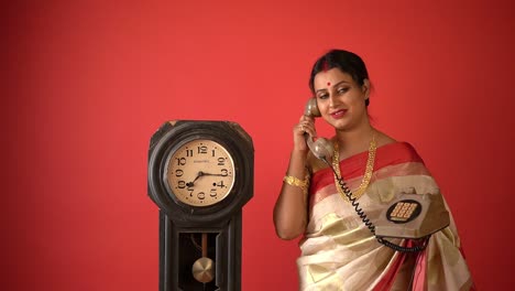 Kolkata:-Traditionell-Gekleidete-Indische-Frau-In-Rot-weißem-Saree-Mit-Einer-Traditionellen-Vintage-Uhr-Und-Einem-Alten-Telefongespräch