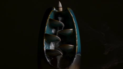 Serene-shot-of-incense-flowing-over-a-ceramic-holder-with-black-a-background