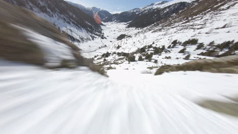 Racing-drone-descending-towards-snowy-valley,-Pyrenees