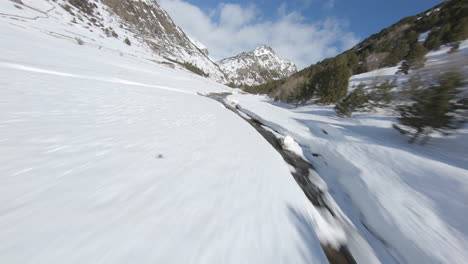 Aerial-drone-fpv-over-stream-flowing-in-snowy-and-frozen-Incles-valley,-Pyrenees