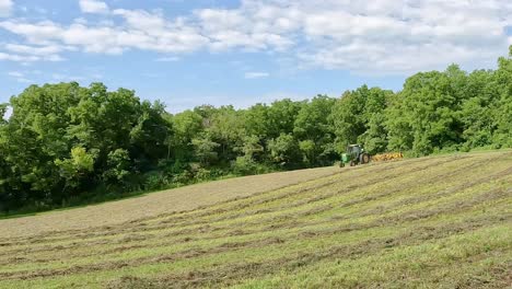 Green-tractor-turning-at-the-end-of-a-row-to-realign-the-hay-rake-to-make-windrows-in-the-cut-and-dried-alfalfa-in-preparation-for-baling-hay