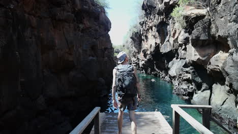Male-With-Backpack-Walking-Towards-Edge-Of-Platform-To-View-Swimming-Pool-At-Las-Grietas-Canyon-In-The-Galapagos