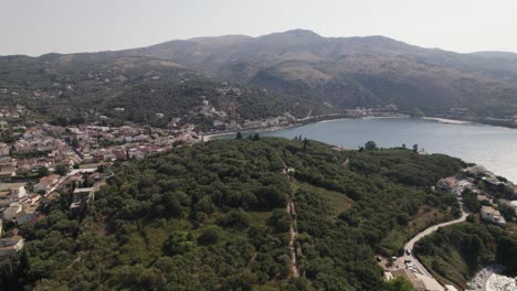 Drone-flyover-Forested-hill-towards-Kassiopi-beach-bay,-Corfu-Island,-Greece,-Cloudy-day