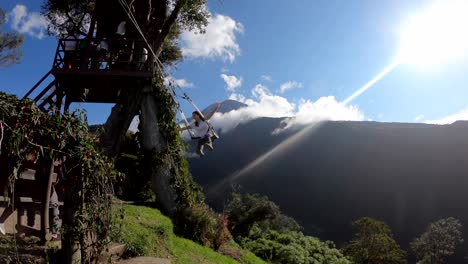 The-Swing-at-the-End-of-the-World-in-Baños,-Ecuador-is-being-visited-by-a-woman-who-is-swinging-while-opening-her-arms-in-happiness
