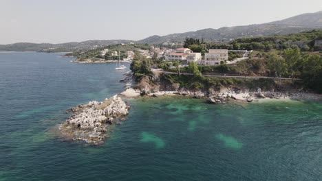 Aerial-view-of-Kassiopi-coastline,-Waterfront-luxury-houses-by-turquoise-sea,-Corfu-Island,-Orbiting