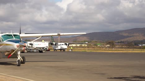 Loading-luggage-onto-turboprop-plane-in-the-runway-near-the-base-of-Mount-Kilimanjaro,-Wide-establishing-shot