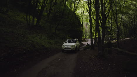 Smooth-aerial-shot-of-the-front-of-an-SUV-driving-uphill-through-calm-forest