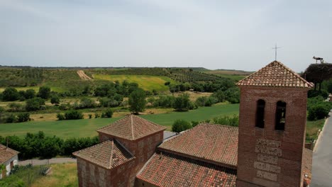 Church-brick-bell-tower-with-stork-nest-and-green-farmlands-in-background