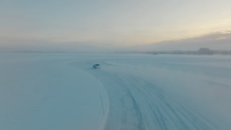 Chasing-speeding-driver-drifting-corners-on-Lapland-ice-lake-aerial-view-at-sunrise