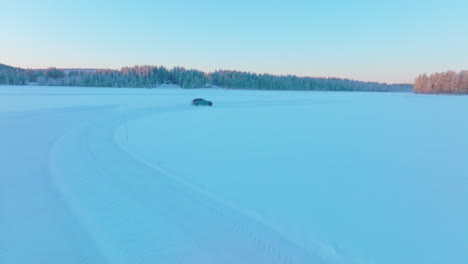Aerial-view-following-drifting-car-speeding-on-Norbotten-woodland-ice-lake-at-sunrise