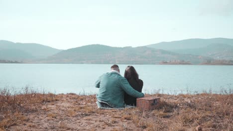 Young-couple-sitting-and-hugging-by-the-riverisde