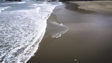 Surfer,-Der-Den-Ozean-Verlässt,-Während-Eine-Drohne-Die-Majestätischen-Szenen-Von-Totoritas-Beach,-Peru,-Enthüllt
