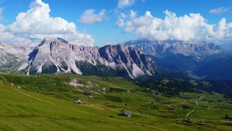 Aerial-view-of-the-depth-of-Val-Gardena-in-Seceda-with-green-pastures,-hiking-trails,-and-huts-in-the-foreground,-and-mountains-in-the-background-in-the-Italian-Dolomites-in-South-Tyrol,-Italy