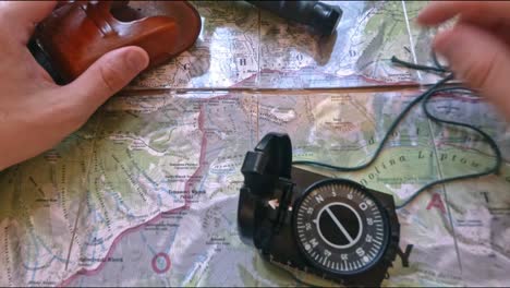 Hitchiker-preparing-to-hike-on-trail-in-mountains-analyzing-the-map-with-a-compass,-pencil-and-knife,-pov,-first-perspective