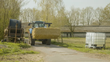 A-tractor-driving-across-a-farm-with-a-massive-block-of-hay