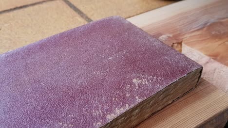 Panning-close-up-to-the-right-on-red-sanding-paper-sitting-on-top-of-wood-plank