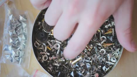 Hand-picking-up-golden-and-silver-pointy-rivets-and-studs-from-a-box-with-multiple-different-ones
