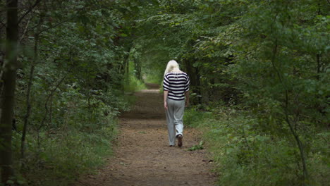 Blonde-haired-woman-is-walking-along-a-forest-path-on-a-sunny-summer-day