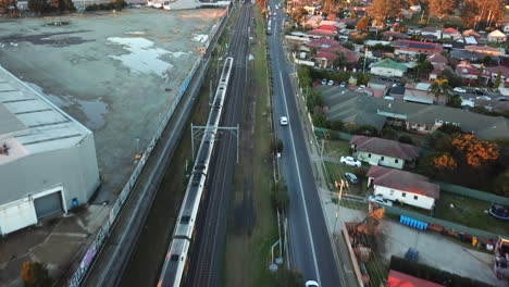 Aerial:-Drone-shot-tracking-a-train-as-it-moves-quickly-through-an-industrial-suburban-area-in-Sydney,-NSW
