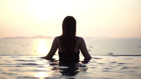 Silhouette-of-woman-in-infinity-pool-overlooking-boats-in-the-sea-at-sunset