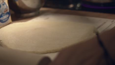 Hand-spreads-flour-and-cuts-dough-with-spatula-in-kitchen,-close-up