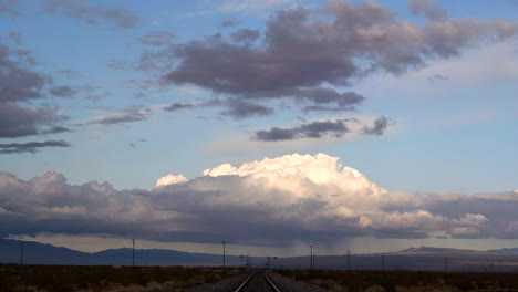 Purple-storm-clouds-roll-through-blue-sky-over-train-tracks-in-desert,-Timelapse