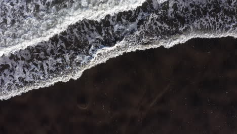 Flying-above-black-sandy-shore-with-waves-crashing-Whatipu-beach,-Huia-Reserve,-NZ