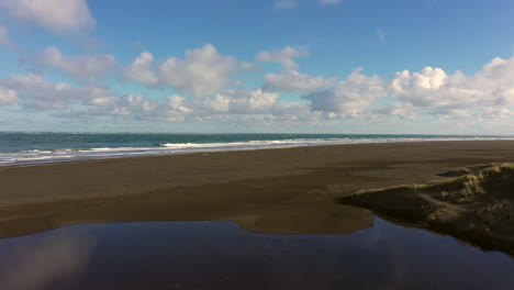 Flying-above-black-sandy-Whatipu-beach-towards-massive-waves,-Huia-Reserve
