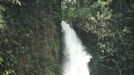 Close-up-view-of-fast-waterfall-flow-going-down-in-Indonesia,-tilt-down