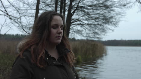 An-unhappy-woman-standing-alone-at-the-lake-and-try-to-hold-herself-to-think-loud-by-touching-her-mouth-with-her-hands-and-wipe-her-tear