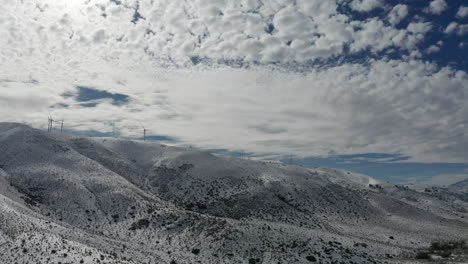 Foothill-mountains-covered-in-fresh-snow-with-clouds-in-sky,-Aerial-Pull-Back