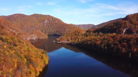 Sliding-drone-shot-of-lake-Tarnita,-Romania,-surrounded-by-colorful-autumn-trees