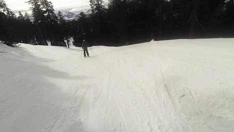 POV-of-Snowboarder-chasing-behind-a-skier-in-a-green-jacket-swooshing-down-a-narrow-trail