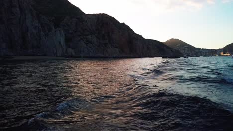 Boat-wake-in-ocean-at-sunset-with-coastal-cliffs-in-background