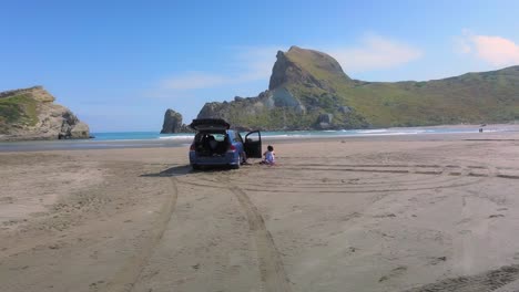 Tracking-shot-of-a-woman-and-blue-van-parked-on-the-beach-at-Castlepoint-in-New-Zealand