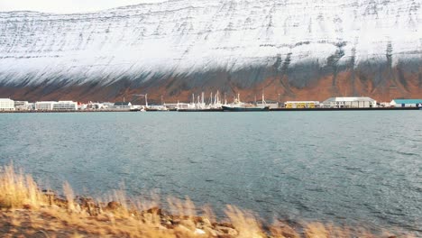 Tiro-Lento-De-Un-Pequeño-Pueblo-En-Islandia-Cerca-Del-Agua-Y-Montañas-Cubiertas-De-Nieve-En-Los-Fiordos-Del-Oeste,-Isafjordur