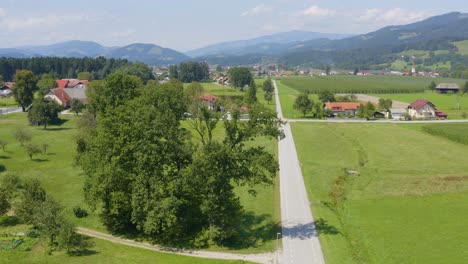 Aerial-view-of-Slovenj-Gradec-town-in-Slovenia-with-tractor,-homes,-farms,-and-roads-below,-Drone-dolly-in-reveal-shot,-license-plates-and-tractor-operator-blurred
