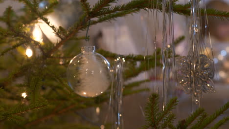 Colgando-Adornos-Navideños-Transparentes-En-Un-árbol-De-Navidad-Real,-De-Cerca