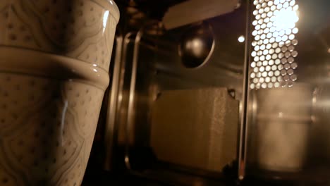 A-painted-cup-spinning-inside-a-microwave,-reflecting-in-one-side