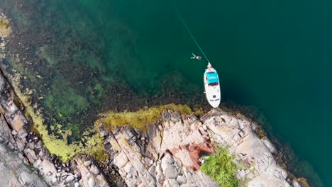 Drone-aerial-descending-flight-towards-small-docked-boat-at-rocky-shoreline-of-Bohuslan,-Sweden