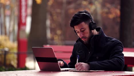 Ein-Mann,-Der-Auf-Seinem-Laptop-Studiert,-Während-Er-Musik-über-Seine-Kopfhörer-Hört---Mittlere-Aufnahme