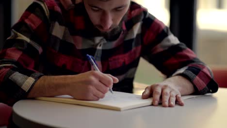 A-young-man-wearing-a-red-and-black-flannel-shirt-writing-notes---Close-up-pan-up-shot