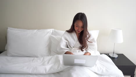 Erfolgreiche-Asiatische-Frau,-Die-Online-Chattet-Und-Mit-Einem-Laptop-In-Einem-Hotelbett-Im-Internet-Arbeitet