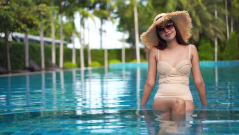 A-smiling-Asian-woman-relaxing-in-a-crystal-blue-swimming-pool,-at-a-luxury-hotel-resort