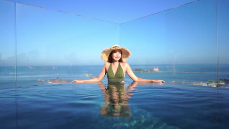 A-cute-Asian-girl-relaxing-in-an-ocean-view-swimming-pool,-at-a-boutique-hotel