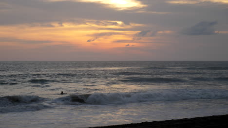 Mann,-Der-Bei-Sonnenuntergang-Herauspaddelt,-Um-Mit-Einer-Frau-Zu-Surfen,-Die-Am-Strand-Vorbeiläuft