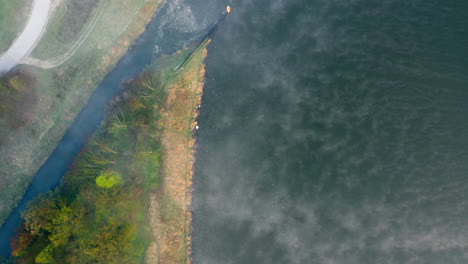 Top-down-aerial-shot-of-a-river-shore,-above-early-morning-fog-clouds