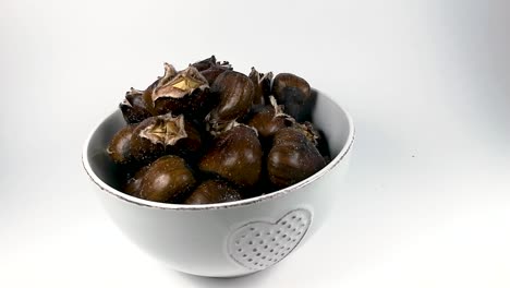 A-hand-picking-up-a-roasted-chestnut-from-a-white-ceramic-bowl,-STILL,-ISOLATED,-SLOMO