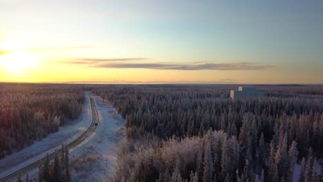 Aerial,-tracking,-drone-shot,-overlooking-a-car-on-a-frozen-road,-in-middle-of-Boreal-forest,-at-sunset,-on-a-sunny,-winter-evening,-in-Gakona,-Alaska,-USA
